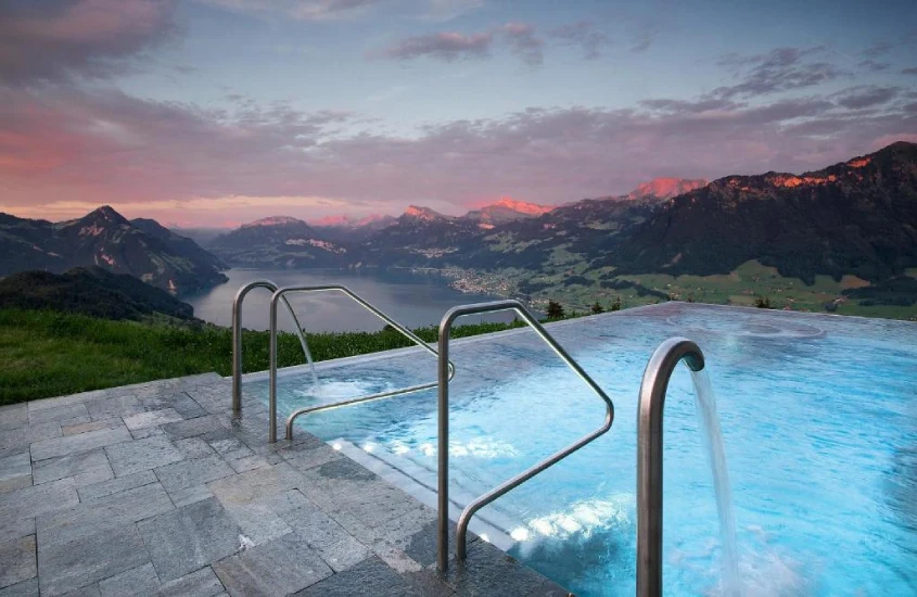 Piscina de borda infinita com vista para montanhas e um lago na Suíça durante o pôr do sol