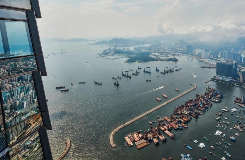 Vista aérea do porto de Hong Kong, com barcos e arranha-céus refletidos nas janelas do hotel