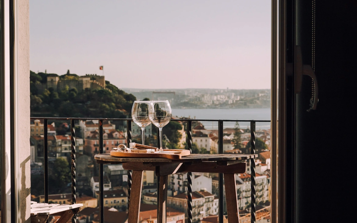 Duas taças de vinho sobre uma mesa com vista panorâmica de uma cidade histórica ao fundo, ao entardecer