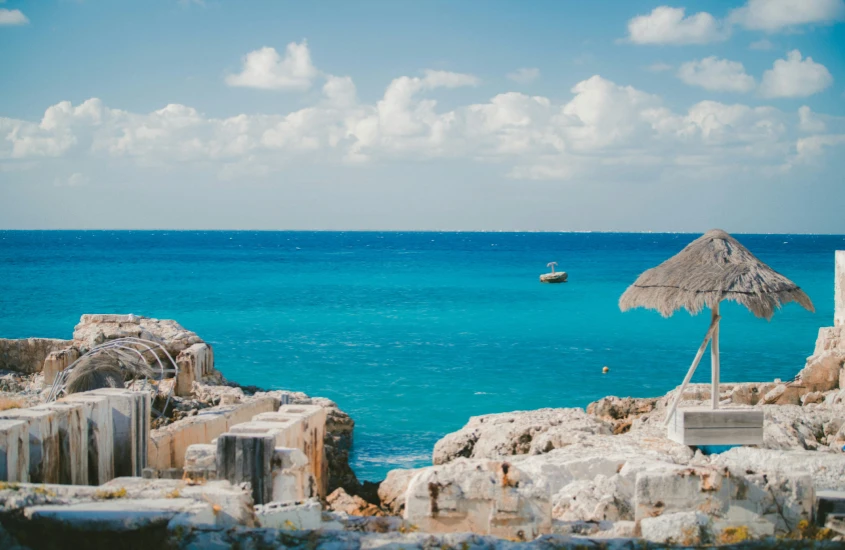 Ruínas de pedra ao lado de um mar azul brilhante em Cozumel, com um céu claro e algumas nuvens no horizonte