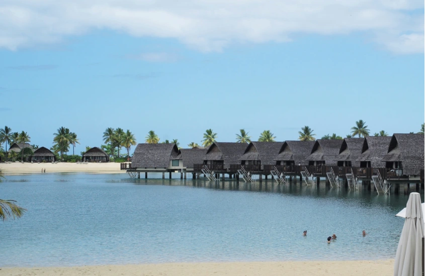 Bangalôs sobre a água em Fiji, com palmeiras ao fundo, cercados por uma lagoa calma e céu azul claro