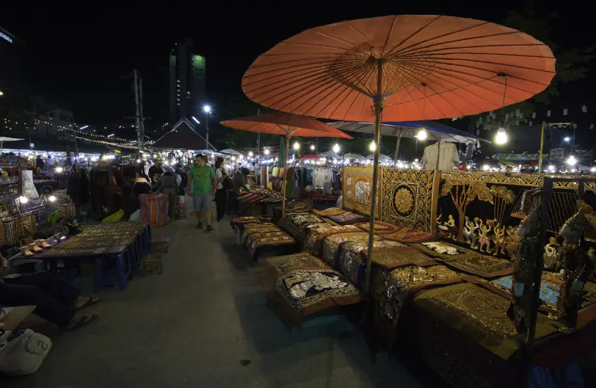 Barracas coloridas no Night Bazaar de Chiang Mai, oferecendo artesanato local e lembrancinhas sob guarda-chuvas tradicionais