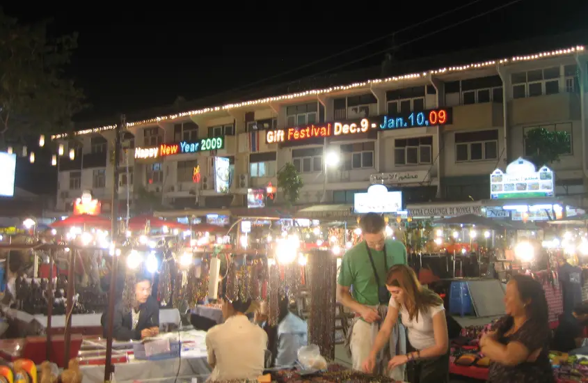 Mercado noturno movimentado em Chiang Mai, com luzes brilhantes e pessoas fazendo compras entre as barracas de lembrancinhas