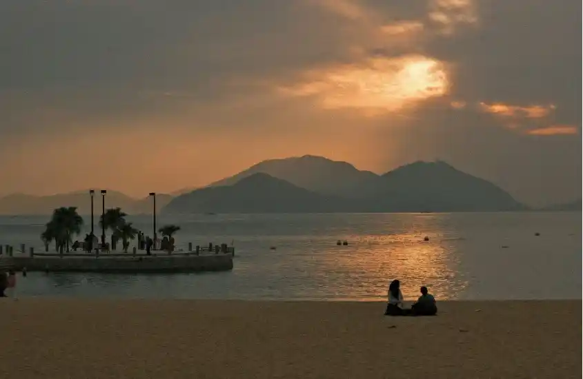 Praia com pôr do sol e montanhas ao fundo