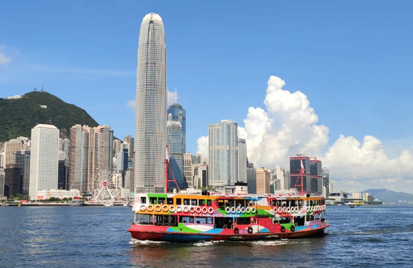 Barco tradicional colorido navegando na baía de Hong Kong com arranha-céus ao fundo