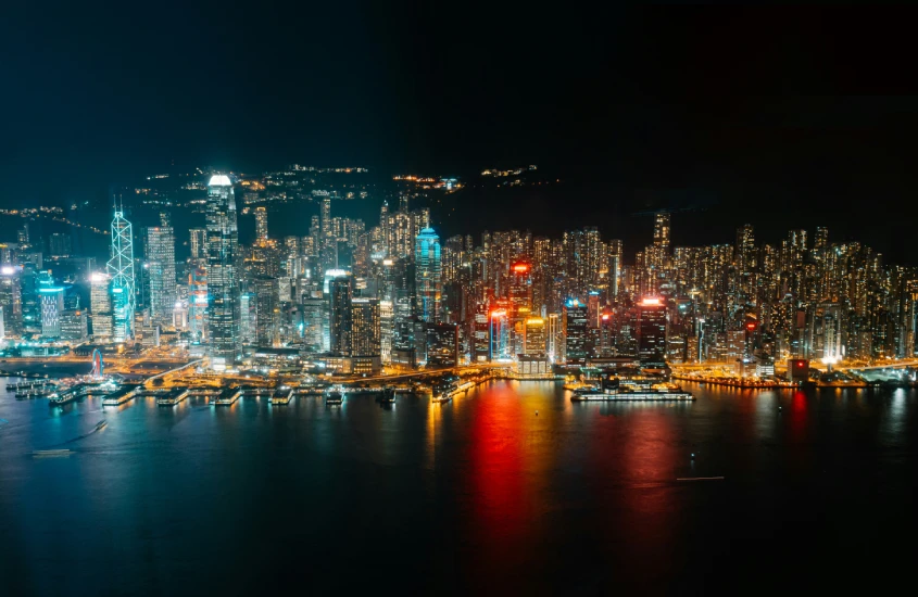 Vista aérea noturna da ilha de Hong Kong, com arranha-céus iluminados refletindo na água