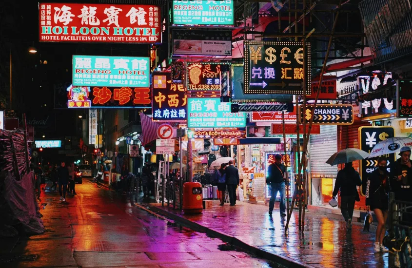 Rua de Hong Kong à noite com letreiros de hotéis e lojas iluminados, sob chuva