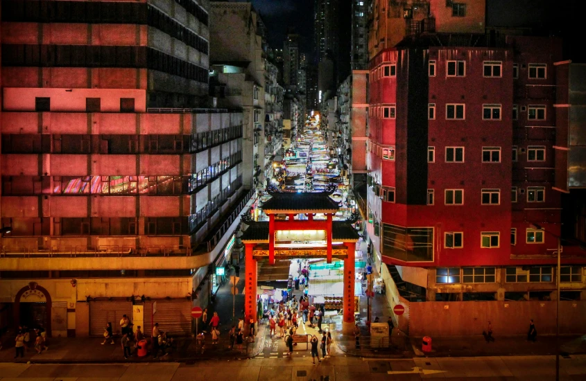 Vista noturna de uma rua movimentada com mercado e prédios iluminados em Hong Kong