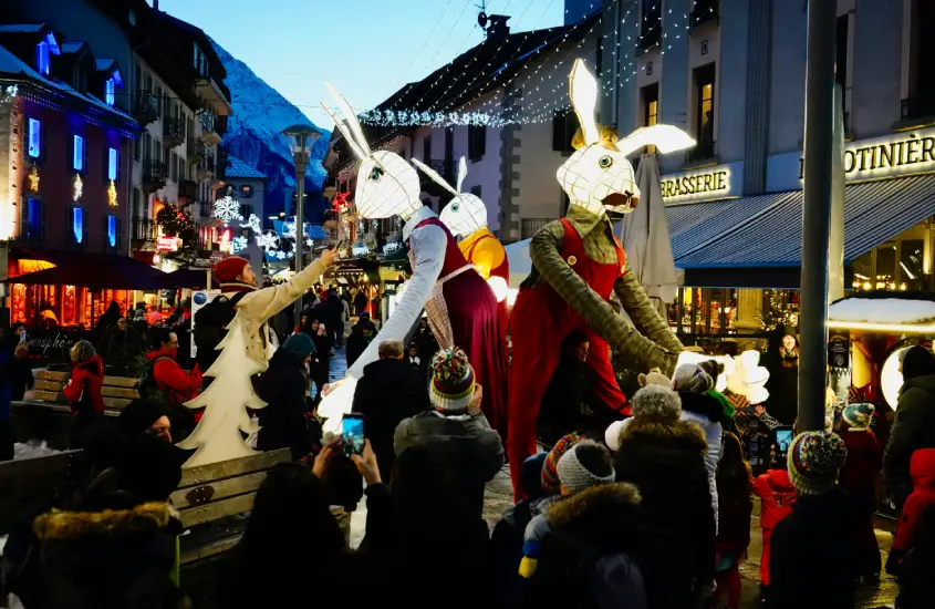 Desfile noturno festivo nas ruas de Chamonix, com figuras de coelhos gigantes e montanhas ao fundo