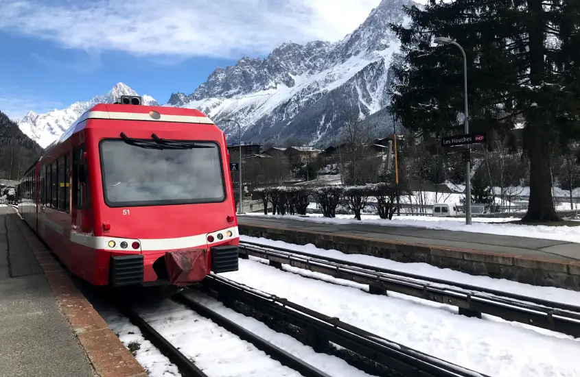 Trem vermelho na estação de Les Houches em Chamonix, com montanhas cobertas de neve ao fundo, durante o dia