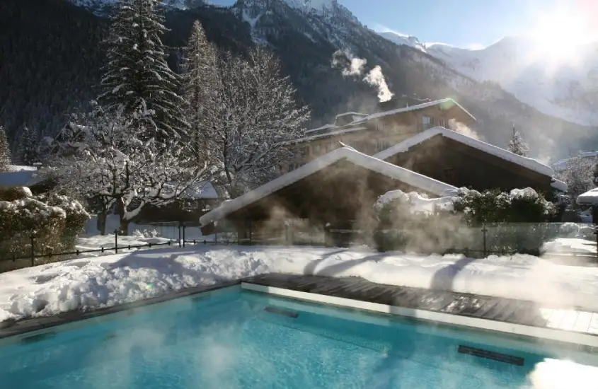 Montanhas cobertas de neve refletidas em um lago cristalino em Chamonix, durante o dia, com um céu azul claro