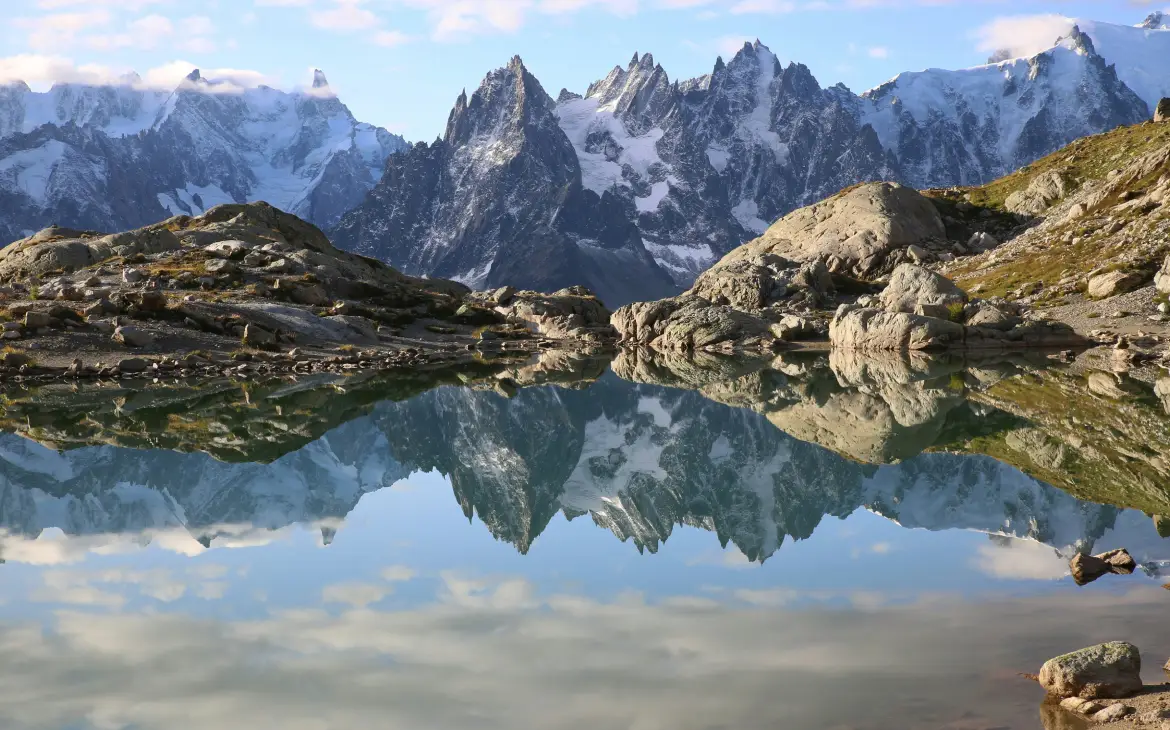 Montanhas cobertas de neve refletidas em um lago cristalino em Chamonix, durante o dia, com um céu azul claro