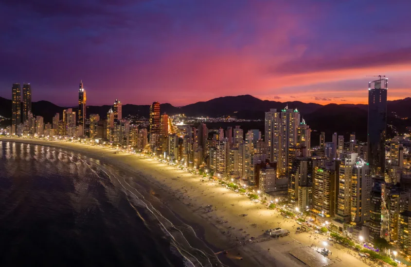 Vista da Praia Central em Balneário Camboriú ao entardecer, com o céu em tons de rosa e roxo.