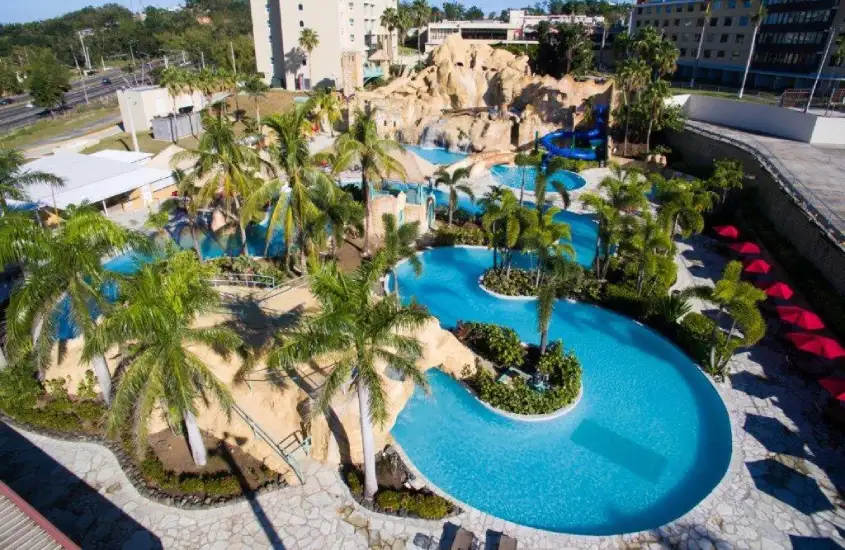 Vista aérea de resort no Caribe com rio lento, piscinas e área de lazer cercada por vegetação