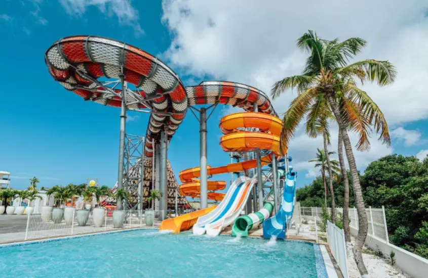 Complexo aquático com toboáguas coloridos, piscina infantil e áreas de lazer em resort cercado por vegetação