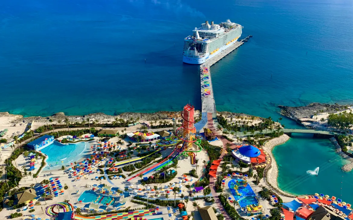 Parque aquático em ilha caribenha com toboáguas, várias piscinas e navio de cruzeiro atracado ao fundo