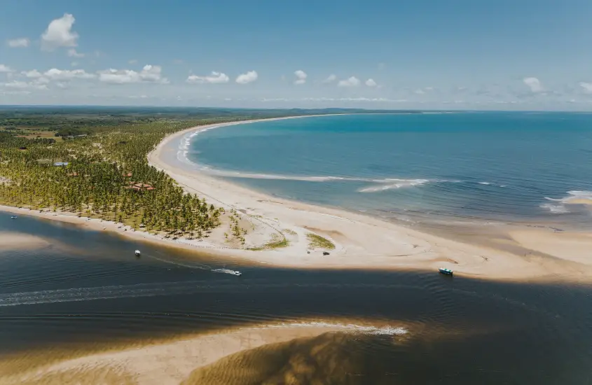 Vista aérea de uma praia paradisíaca com uma extensa faixa de areia, água azul-turquesa e vegetação densa ao fundo