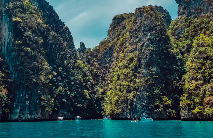 Barcos ancorados em uma baía cercada por penhascos altos e vegetação em Koh Phi Phi durante o dia