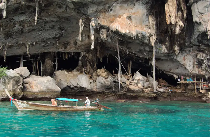 Entrada da Viking Cave com um longtail boat ancorado na água azul-turquesa em frente à caverna durante o dia