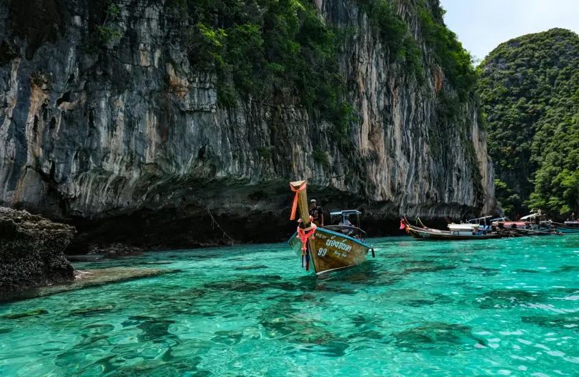 Longtail boat na água cristalina perto de um penhasco de calcário em Koh Phi Phi durante o dia