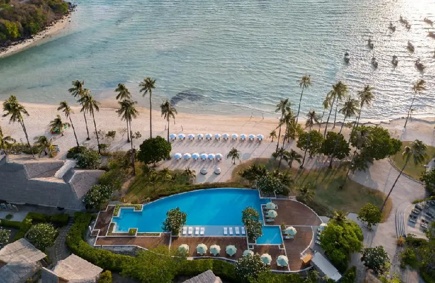 Vista aérea do SAii Phi Phi Island Village, mostrando a piscina ao ar livre, palmeiras e a praia com águas azul-turquesa durante o dia