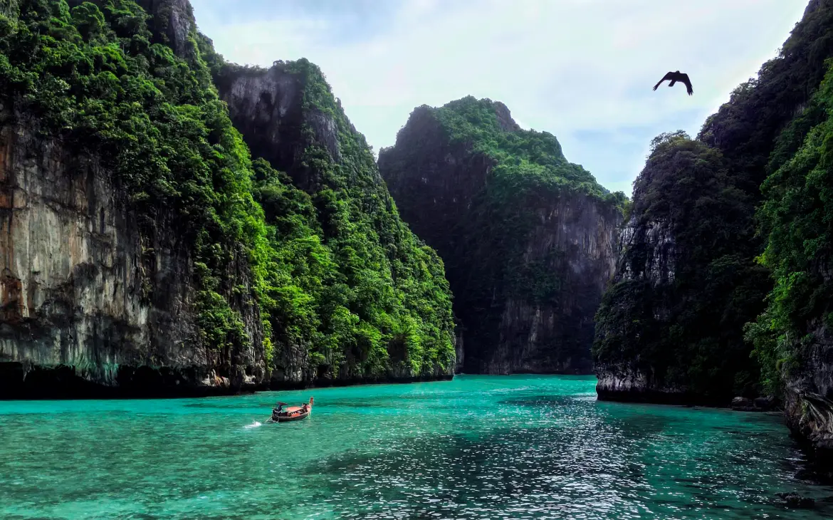 Longtail boat navegando em águas azul-turquesa cercadas por penhascos cobertos de vegetação em Koh Phi Phi durante o dia