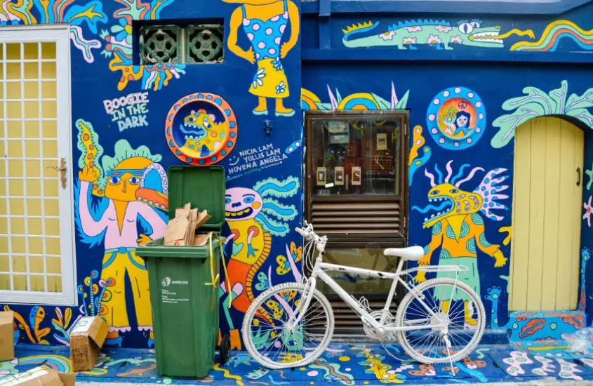 Mural de grafite colorido em Haji Lane, Singapura, com uma bicicleta branca encostada na parede, visto durante o dia.