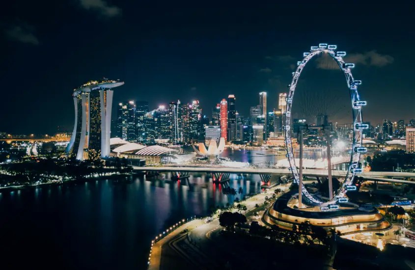 Vista noturna do skyline de Singapura com a Singapore Flyer iluminada e o Marina Bay Sands ao fundo.