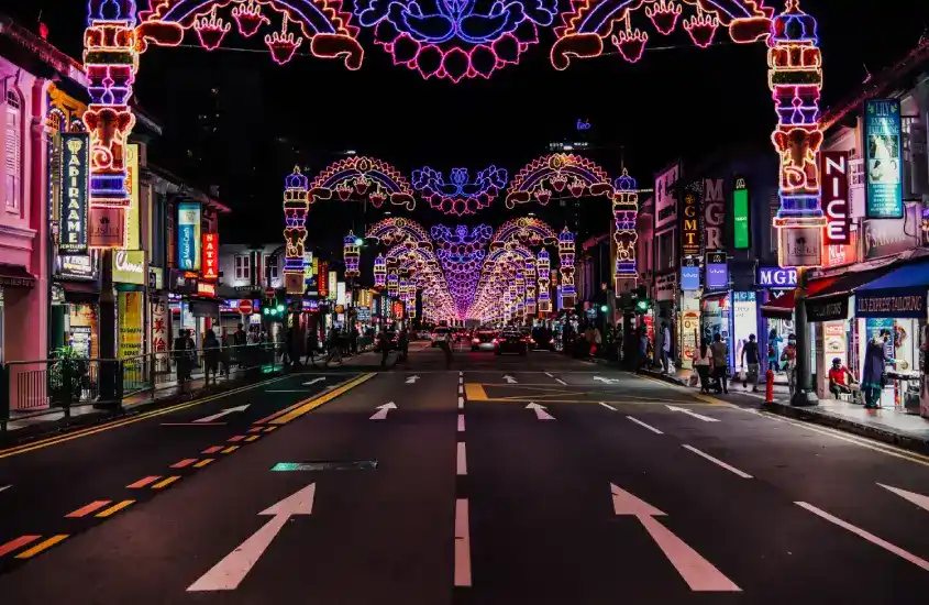 Rua principal de Little India, Singapura, iluminada à noite com decorações coloridas e letreiros de lojas.