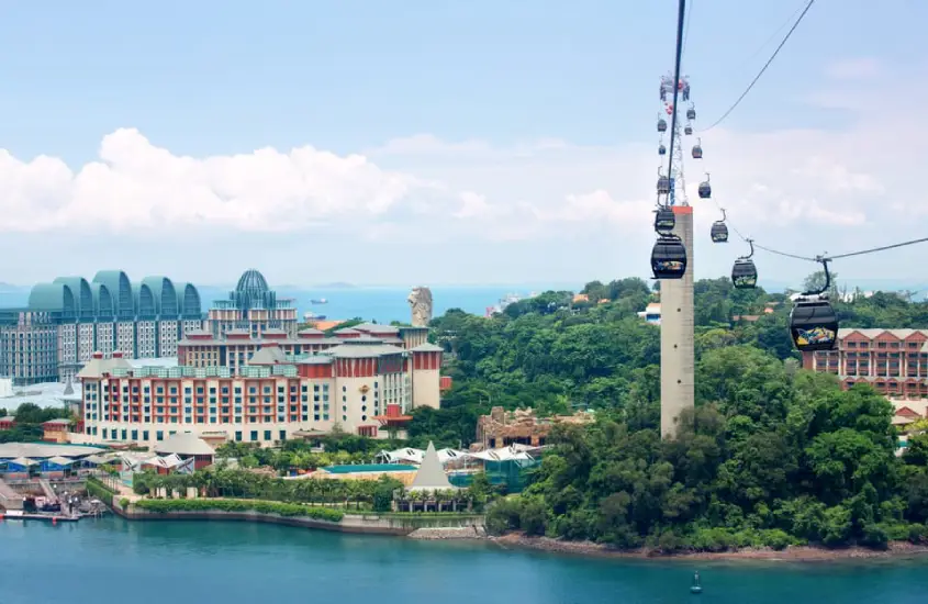 Cabines do teleférico conectando a ilha principal de Singapura à ilha de Sentosa, durante o dia, com vista para resorts e vegetação.