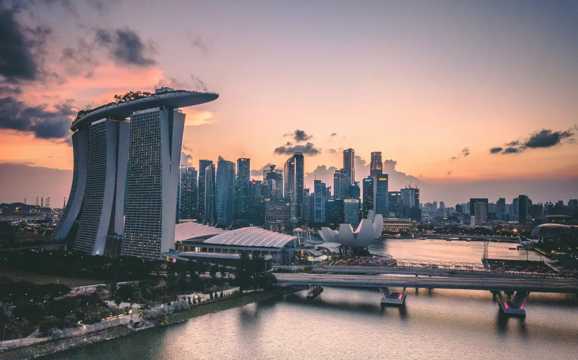 Vista aérea do Marina Bay Sands e do skyline de Singapura ao entardecer, com o céu alaranjado e reflexos no rio