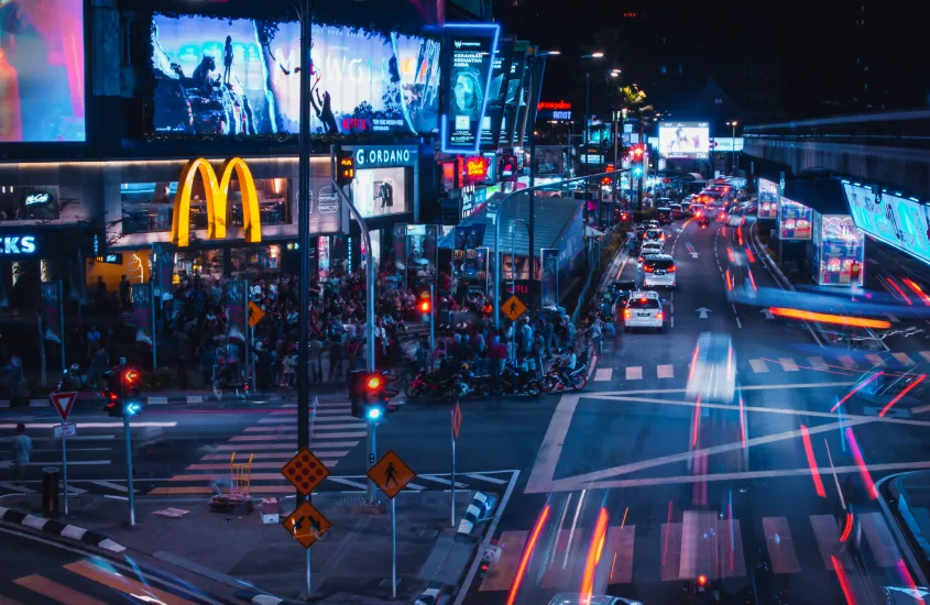 Cena noturna de uma avenida movimentada em Bukit Bintang, com fachadas iluminadas de lojas e restaurantes