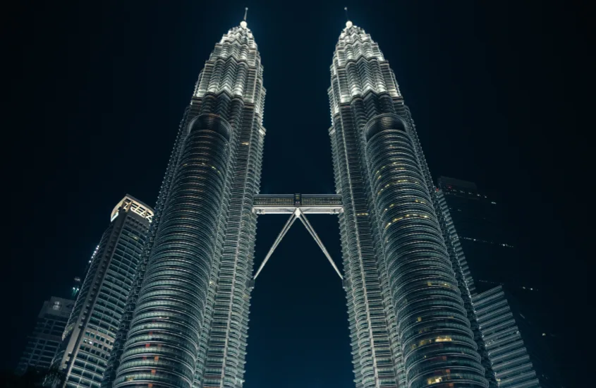 Torres Petronas iluminadas à noite, com foco no Skybridge conectando os dois edifícios