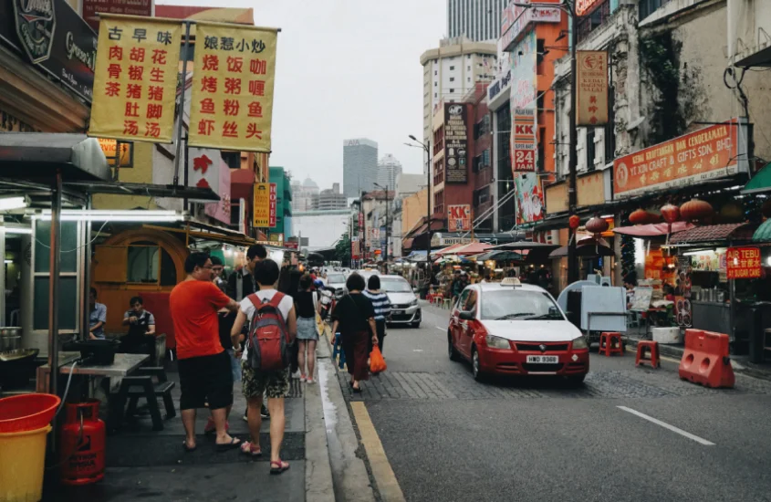 Rua movimentada em Kuala Lumpur com vendedores ambulantes e lojas com letreiros em chinês