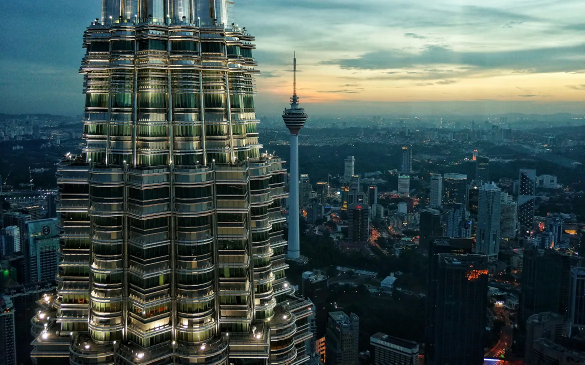 Vista aérea das Torres Petronas ao entardecer, com a Torre de Kuala Lumpur ao fundo