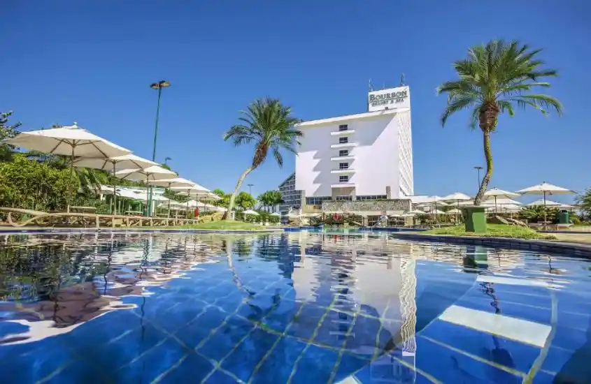 Vista da piscina de resort de luxo durante o dia, com o céu azul refletido na água cristalina