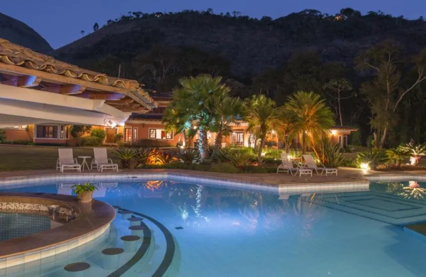 Piscina iluminada ao entardecer, com montanhas ao fundo e a luz suave do início da noite, em um dos resorts mais luxuosos do Brasil