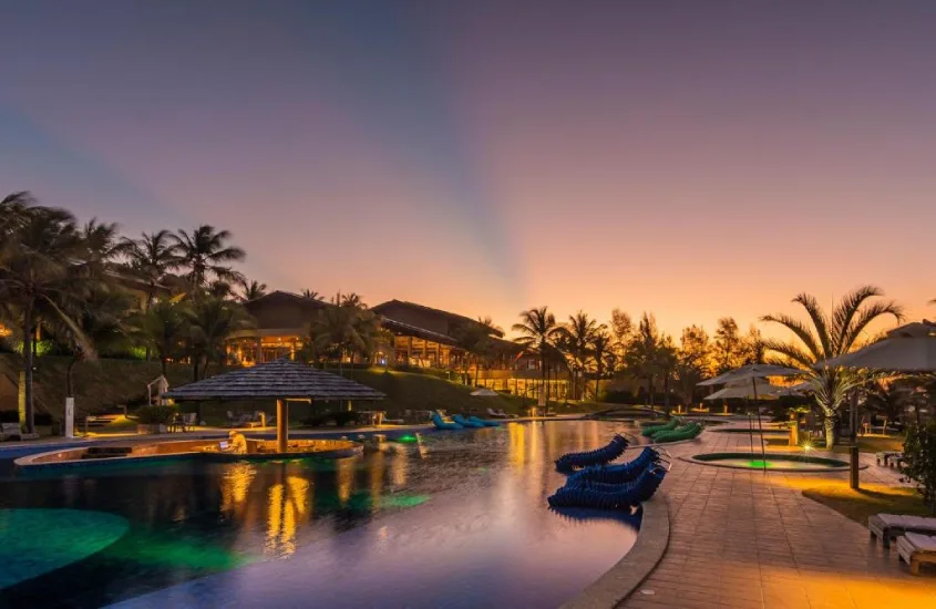 Piscina iluminada ao entardecer em resort de luxo cercado por palmeiras