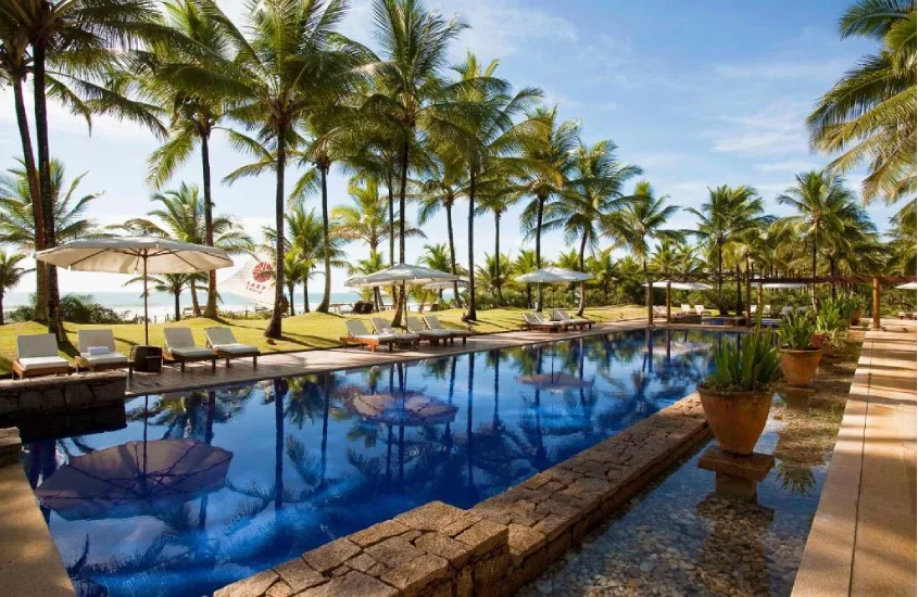 Piscina de um resort de luxo rodeada por espreguiçadeiras e jardins tropicais à tarde