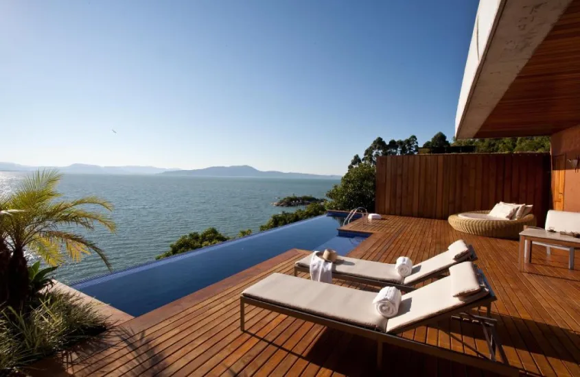 Deck de madeira com espreguiçadeiras, piscina e vista para o mar em villa de resort de luxo, durante o dia