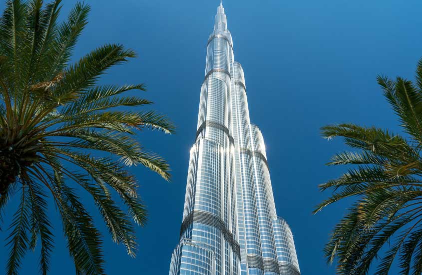 Vista do Burj Khalifa em Dubai, o edifício mais alto do mundo, com palmeiras ao fundo.