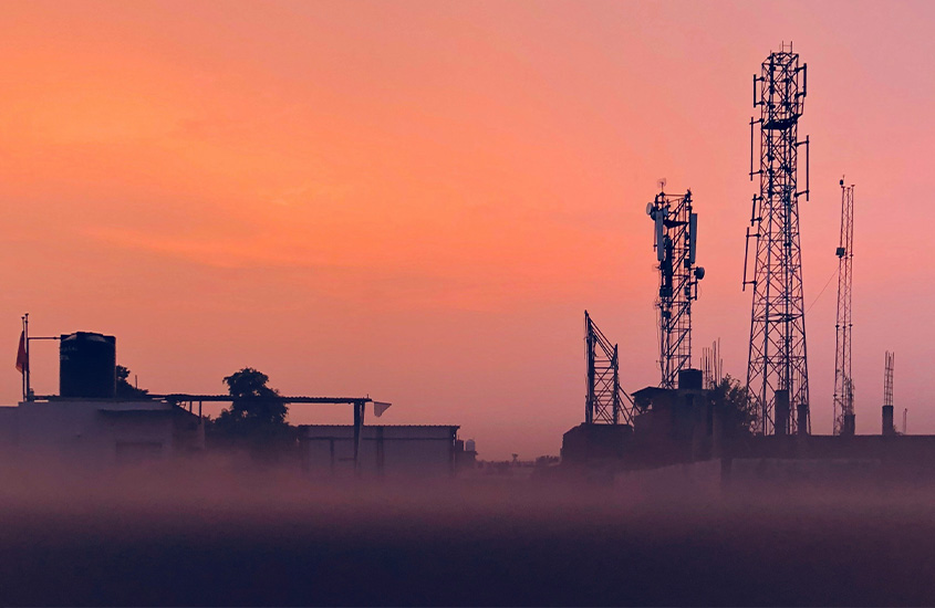 Silhuetas de torres de telecomunicações contra um céu laranja vibrante ao anoitecer.