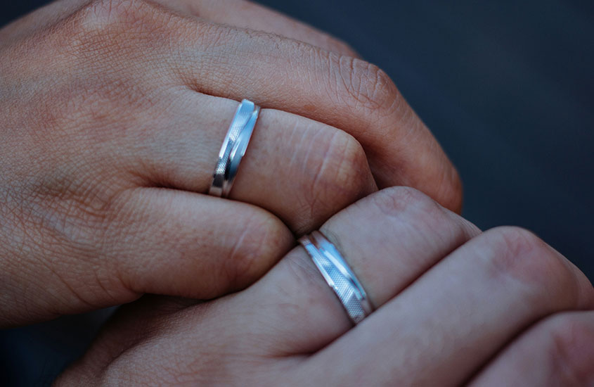 Duas mãos juntas, cada uma com uma aliança de casamento prateada, simbolizando o compromisso.