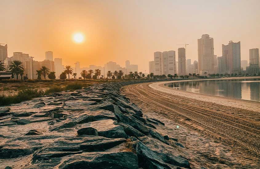 Um pôr do sol sobre uma praia com arranha-céus ao fundo, mostrando o contraste entre a natureza e a urbanização.