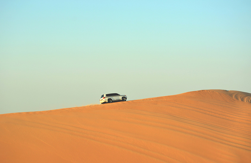 Um carro 4x4 solitário navega pelas vastas dunas de areia do deserto dos Emirados Árabes Unidos.