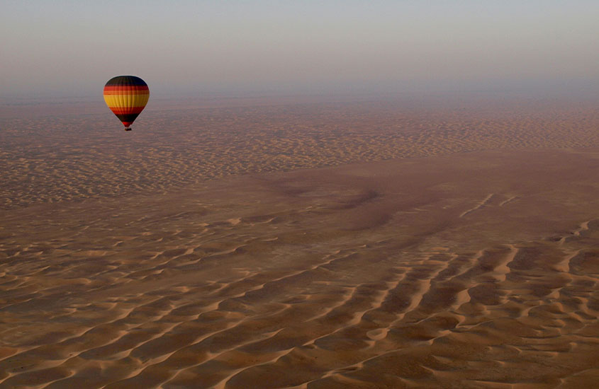 Um balão de ar quente flutua sobre as vastas e ondulantes dunas do deserto ao amanhecer.