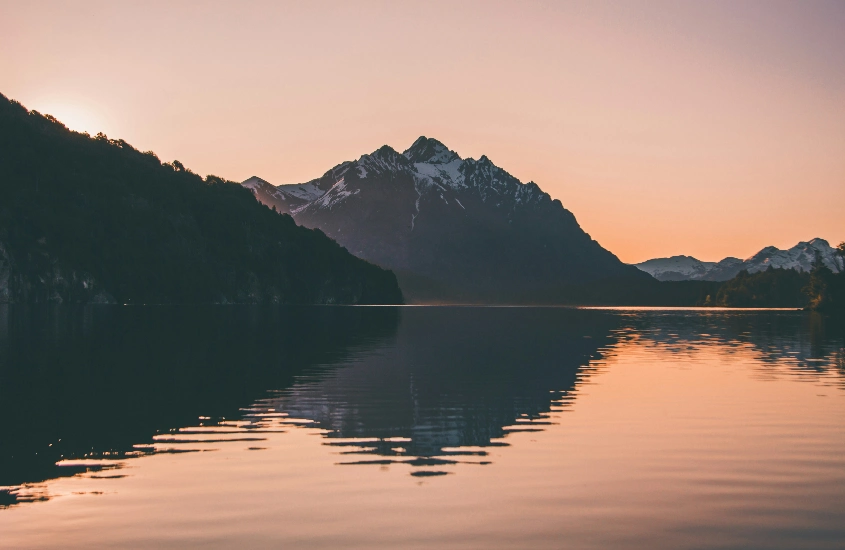 Montanhas ao fundo e o sol se pondo sobre um lago calmo, em Bariloche, um dos destinos de inverno que não dá pra deixar de visitar