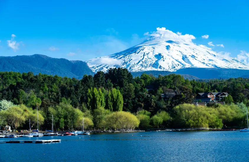 O vulcão Villarrica, coberto de neve, com um cenário verde e azul ao redor, em Pucón, um dos destinos de inverno mais incríveis do Chile