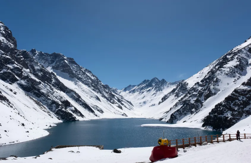 Lago glacial cercado por montanhas nevadas e céu azul em Portillo, um destino de inverno famoso entre os esquiadores