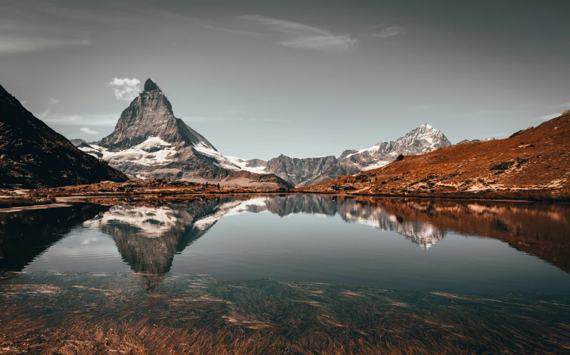 A imponente montanha Matterhorn reflete nas águas tranquilas de um lago, com picos nevados ao redor, em Zermatt, um dos melhores destinos de inverno do mundo